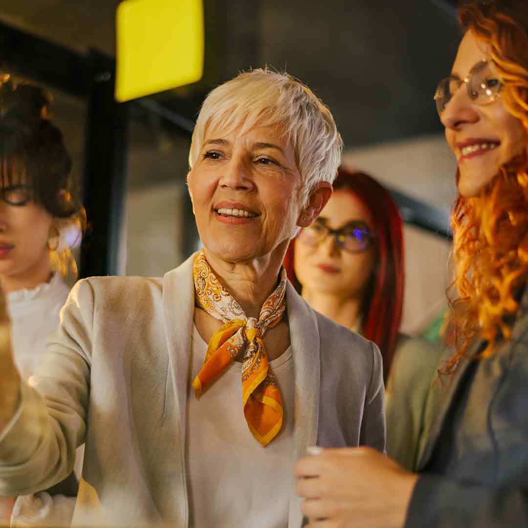 Manager and staff in funky business attire talking in front of a glass window post it notes on it.