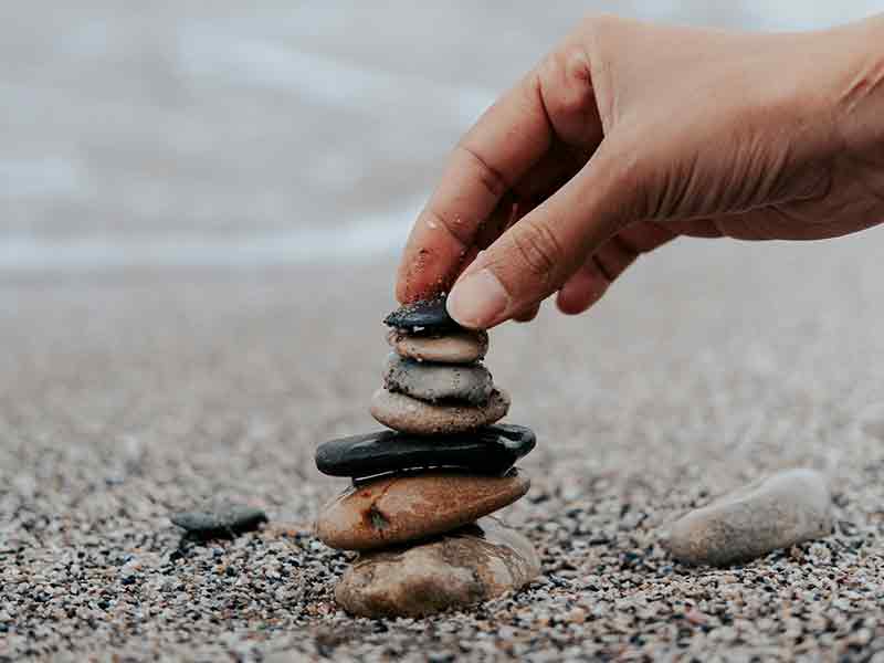 a hand stacking pebbles on a beach with water in the background
