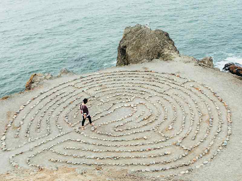 Person walking a rock labyrinth on a sand cliff top by the coast