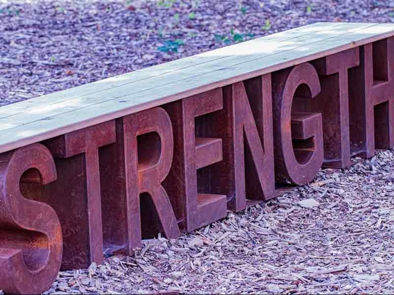 A wooden bench plank supported by metallic letters that spell strength