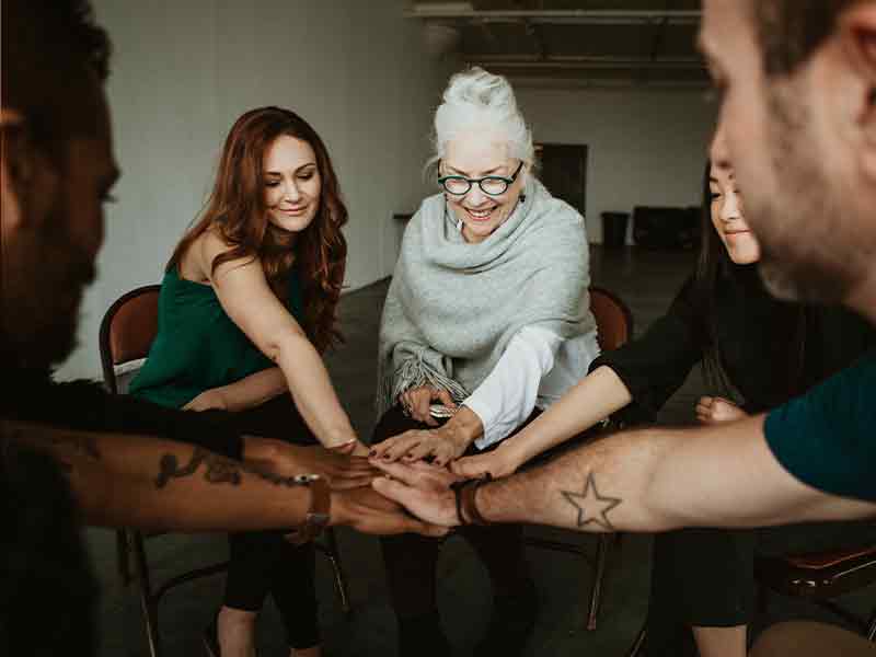 people sitting in circle in trauma-informed co-design workshop with hands outstretched and overlapping in the center
