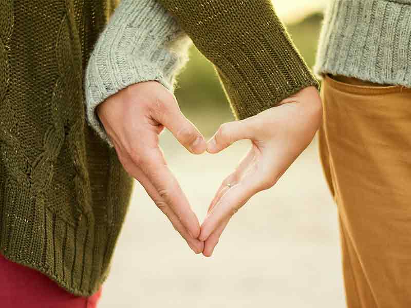 Two people's hands help together to make the shape of a heart